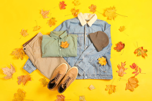 Chaqueta de mezclilla, pantalones, camisa, sombrero, zapatos y hojas de otoño sobre fondo de color - Foto, imagen