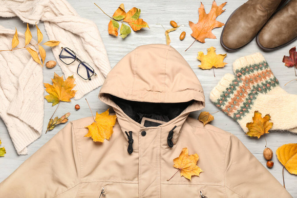 Stylová bunda, šála, brýle, boty, ponožky a podzimní listí na světlém dřevěném pozadí - Fotografie, Obrázek