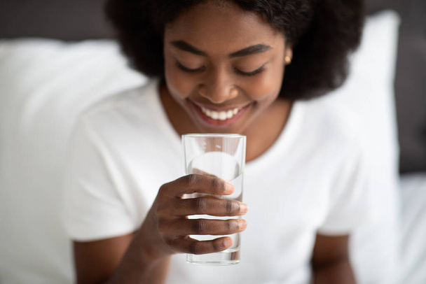 Fiatal fekete nő vesz pohár vizet az ágyban - Fotó, kép