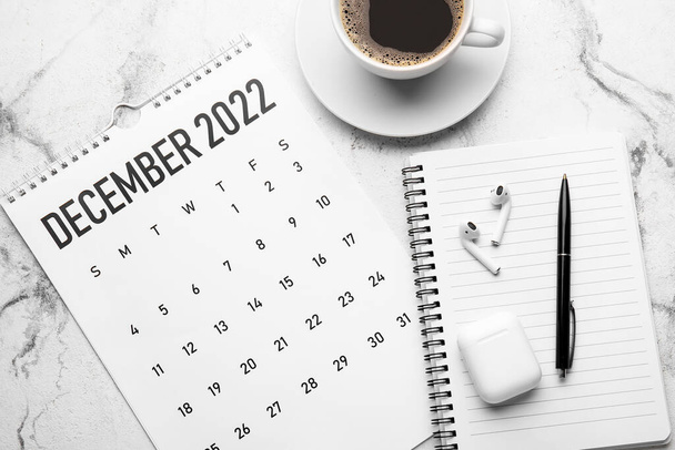 Kalendarz papierowy na grudzień 2022 r., notatnik, długopis, słuchawki i filiżanka kawy na jasnym tle - Zdjęcie, obraz