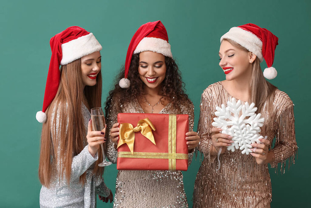Beautiful young women in Santa hats, with Christmas gift and champagne on color background - Foto, Imagen