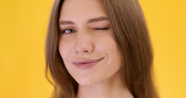 Hravá koncepce nálady. Detail portrét mladé veselá žena mrkající a široce se usmívající na fotoaparát, žluté pozadí - Záběry, video