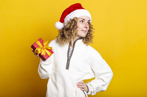 Smiling young woman in santa claus hat with gift box on yellow background - Foto, Imagem