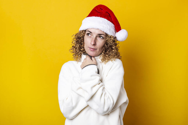 Curly young woman in santa claus hat on a yellow background - Foto, Bild