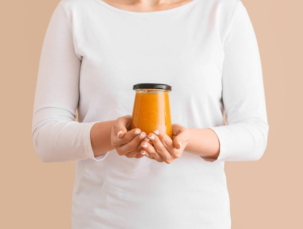 Woman holding jar of tasty tangerine jam on color background - Photo, Image