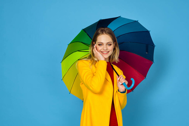 woman in yellow coat multicolored umbrella posing blue background - Fotoğraf, Görsel
