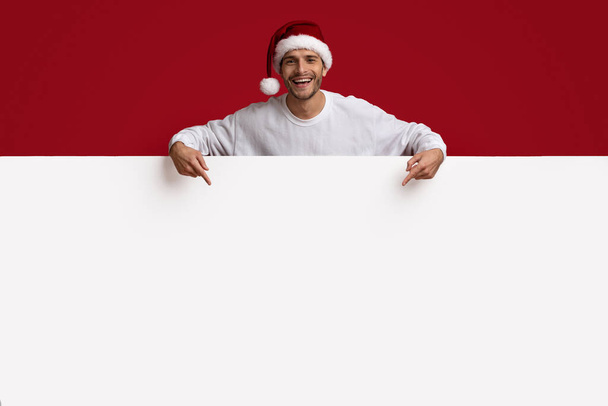 Annonce de Noël. Guy excité pointant vers le bas au panneau blanc de publicité avec des doigts - Photo, image