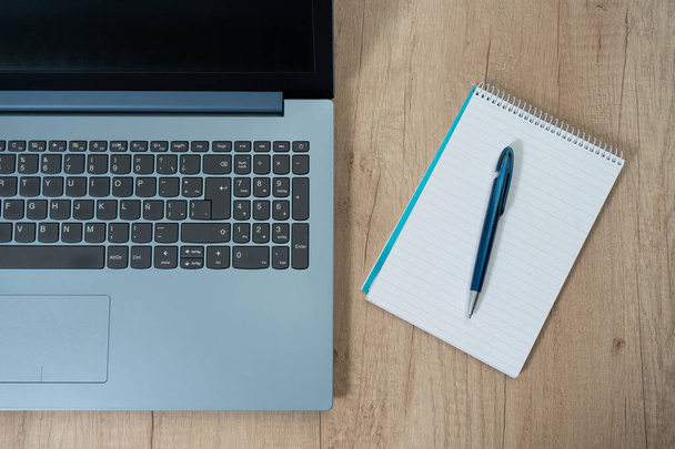 Una computadora portátil junto a un bloc de notas en blanco y un bolígrafo en una mesa de trabajo. Tecnología, comunicaciones, concepto de oficina en casa - Foto, imagen