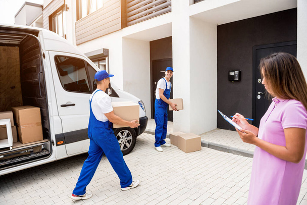 Twee verhuisbedrijf werknemers lossen dozen van minibus in klanten thuis - Foto, afbeelding