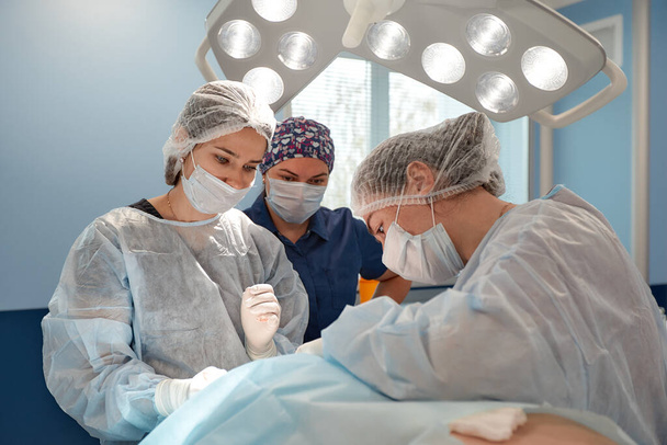 Konsantre cerrahi ekibi ameliyathanede bir hastayı ameliyat ediyor. Karmaşık makinelerle yıllarca eğitim almış iyi eğitimli bir anestezi uzmanı ameliyat boyunca hastayı takip eder. - Fotoğraf, Görsel