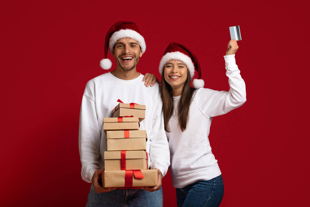 クリスマスショッピング。クレジットカードとギフトのスタックを持つ幸せな若いカップル - 写真・画像
