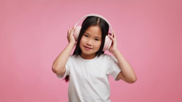 Корейська дівчинка, яка слухає музику, носить навушники через рожеве тло - Кадри, відео