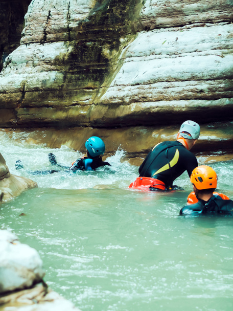 Tři muži v helmách a neoprénech plují po řece, která teče mezi kaňony. Extrémní dovolená. Kaňon - Fotografie, Obrázek