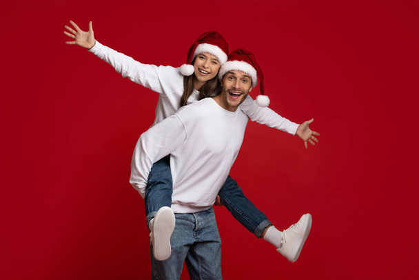 Šťastné svátky. Veselý pár v Santa klobouky Bavit se nad červeným pozadím - Fotografie, Obrázek