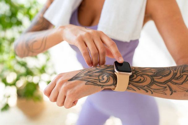 Jonge getatoeëerde vrouw op zoek naar activiteit fitness tracker tijdens de training pauze, het controleren van de hartslag en verbrande calorieën - Foto, afbeelding