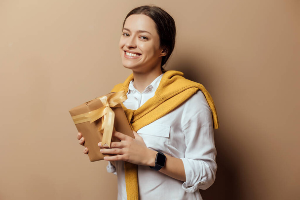 Young woman in white shirt hold christmas handmade present packed in kraft paper on epmty wall background - Photo, Image