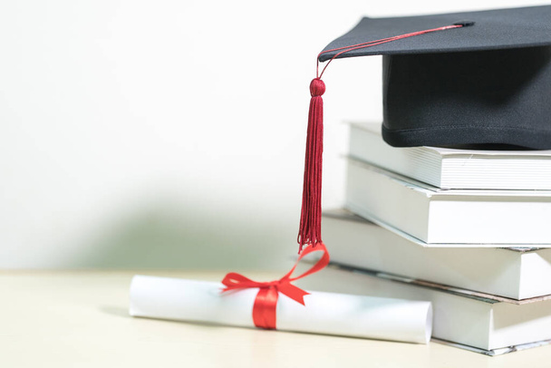 A closeup shot of a certificate, and a mortarboard on a stack of books on a white table background - Foto, immagini