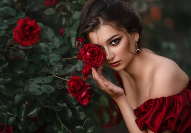 Beautiful woman in red dress walking in the garden full of roses. - Φωτογραφία, εικόνα