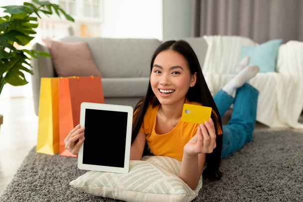 Щаслива азіатська жінка показує планшет з порожнім екраном і кредитною карткою, покупки в веб-магазині, демонструє макет
 - Фото, зображення
