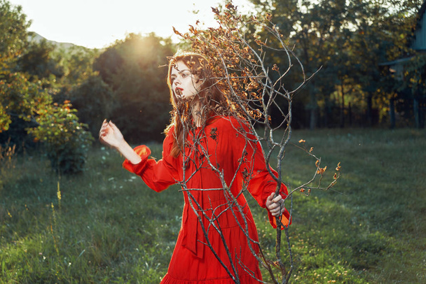 woman in red dress in field near tree posing summer - Фото, изображение