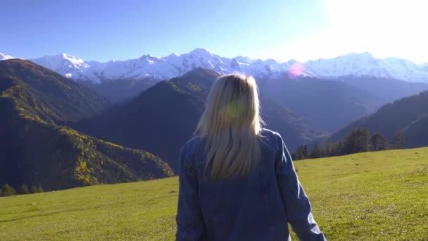 Bir kadın çayırda oturuyor ve dağların manzarasının tadını çıkarıyor.. - Video, Çekim