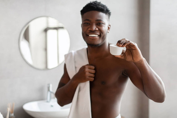 afro-américain mâle montrant visage crème pot posant dans salle de bain - Photo, image