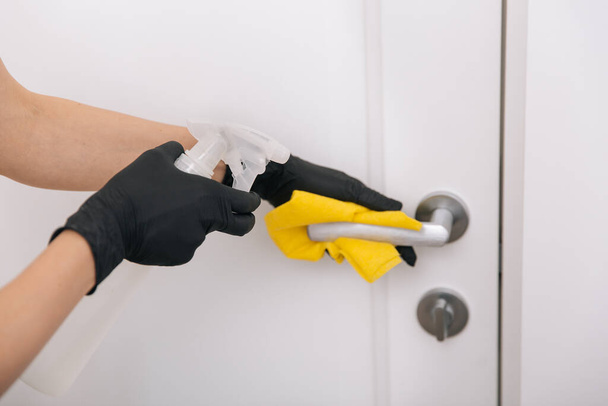 Cleaning door handle with yellow wipe in black gloves and sanitizer spray. Disinfection in hospital and public spaces against corona virus. Woman hand using towel for cleaning - Photo, Image