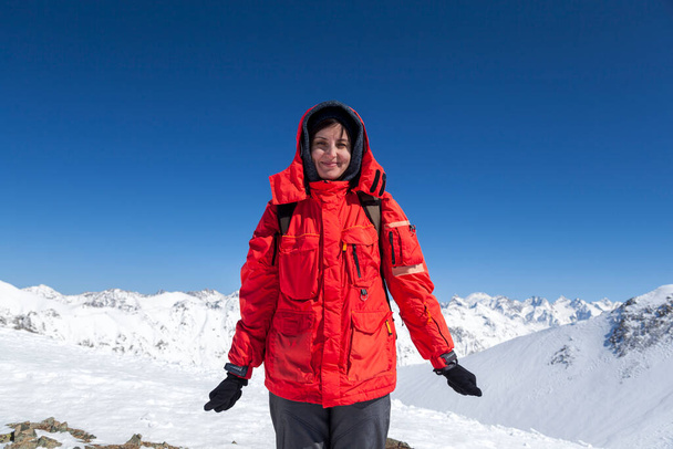 Ein schönes brünettes Mädchen in einem Skigebiet, vor dem Hintergrund der Kaukasusberge, blickt auf die Gipfel der Berge - Foto, Bild
