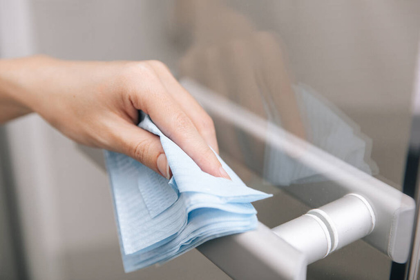 Cleaning glass door handles with an antiseptic wet wipe. Woman hand using towel for cleaning home room door link. Sanitize surfaces prevention in hospital and public spaces against corona virus - Valokuva, kuva