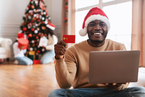 Compras en línea de Navidad. Sonriente usando laptop mostrando tarjeta de crédito - Foto, imagen