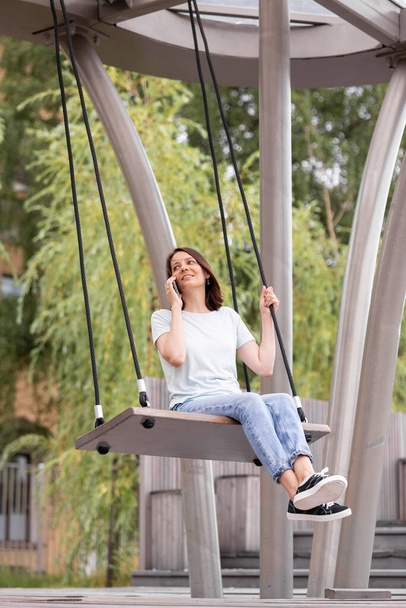 a young and confident woman blogger or marketer is talking on the phone and riding a swing - Photo, image