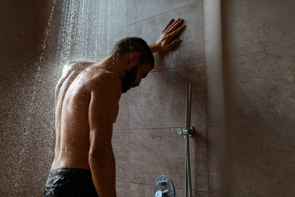 Genç adam modern banyoda duş alıyor. - Fotoğraf, Görsel