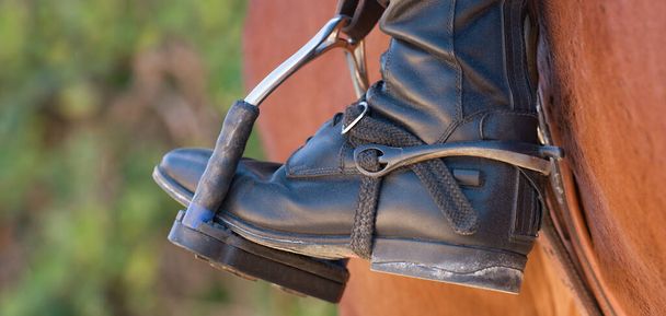 Der Fuß des Athleten in einem Steigbügel auf einem Pferd, der Fuß des Reiters, sitzend auf einem Pferd, in einem schwarzen Stiefel mit Sporn, ruht auf einem Metallbügel - Foto, Bild