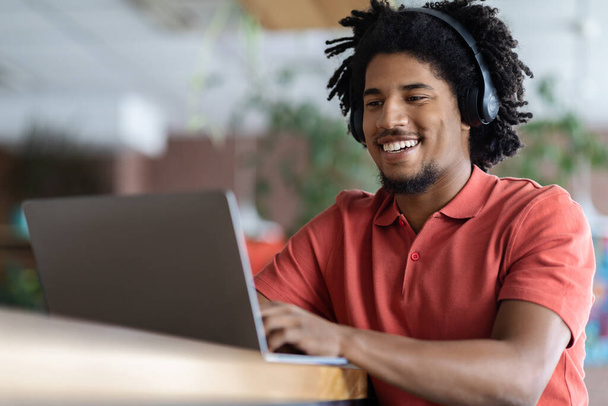 Joyful Young Black Guy In Wireless Headphones Using Laptop In Cafe - Photo, Image
