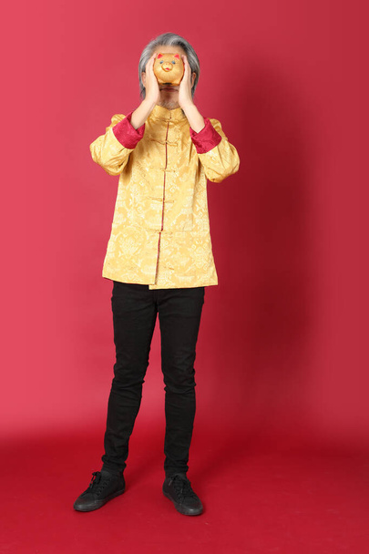The senior Asian man wearing traditional gold chinese dresses standing on the red background. - Foto, Bild
