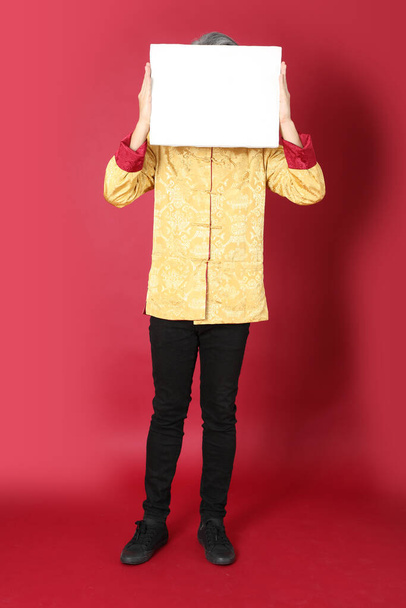 The senior Asian man wearing traditional gold chinese dresses standing on the red background. - Photo, Image