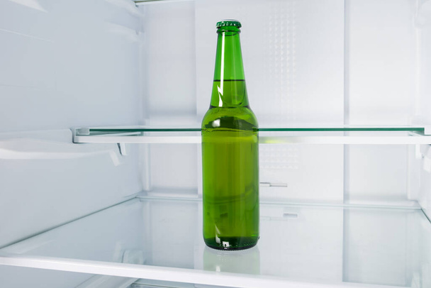 a bottle of beer on a shelf in an empty refrigerator - Фото, зображення
