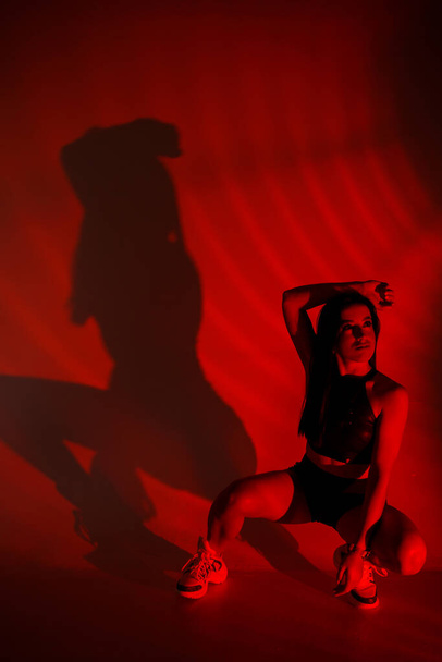Servizio fotografico di una giovane bruna in uno studio fotografico. Bella donna snella in un top nero e pantaloncini a luce rossa. - Foto, immagini