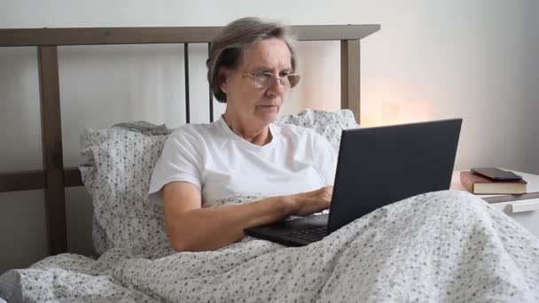 Hlavní předmět je rozostřený, stará stárnoucí seniorka v posteli byt pracuje doma kancelář drží notebook pracovních míst pro důchodce, obsahuje hluk - Záběry, video