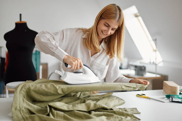 Costurera suaviza la tela con una plancha, taller - Foto, imagen