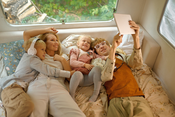 Cheerful family lying in bed in motorhome, camping - Φωτογραφία, εικόνα