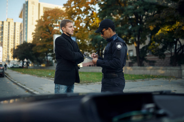 Αστυνομικός αστυνομικός επιβάλλει πρόστιμο στον άντρα οδηγό. - Φωτογραφία, εικόνα