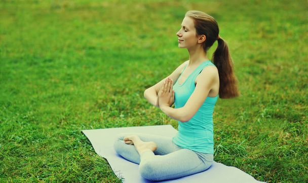 Young woman doing yoga exercises on a mat on the grass in summer park - Foto, imagen