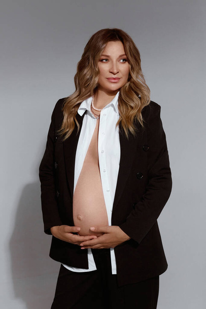 Gorgeous young pregnant woman in black suit with with bare tummy - Φωτογραφία, εικόνα