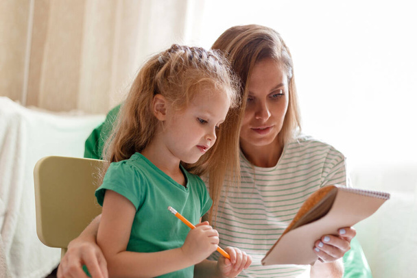 Caucasian blonde smart child kid 5 years do homework Learn to write with mom 30s together. Mother helps preschooler girl daughter to do homework. Homeschooling and Kindergarten Concept - Photo, image