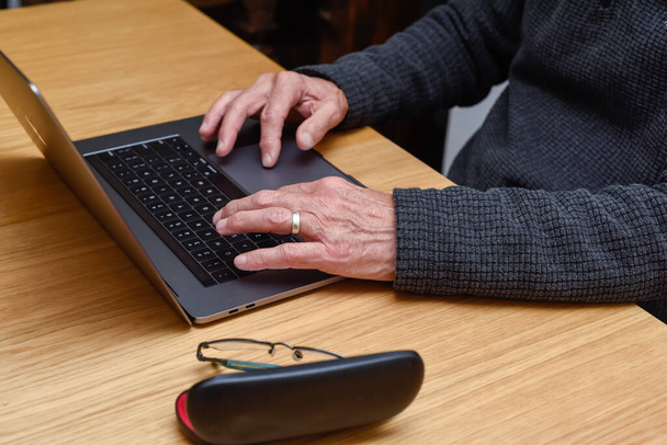 Senior Man met laptop thuis met close-up detail op handen op het toetsenbord - Foto, afbeelding