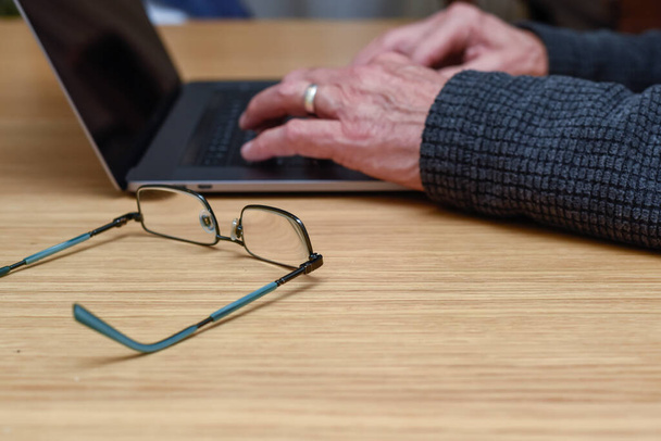 Homme âgé utilisant un ordinateur portable à la maison avec des détails de gros plan sur les mains sur le clavier - Photo, image