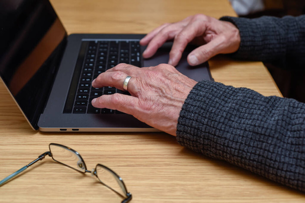 Senior Man using laptop at home with close up detail on hands on keyboard - 写真・画像