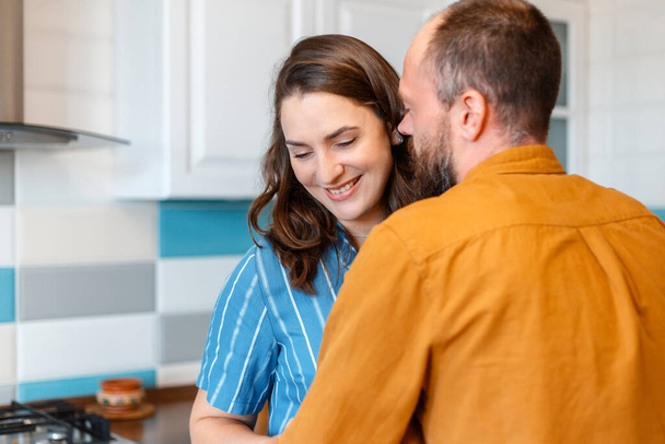 Happy young loving couple man woman 30s in kitchen at home. Married couple Wife and husband hugging having fun Smiling kiss In kitchen interior of apartment. - Foto, Imagem