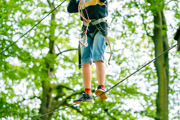 森の冒険公園の学校の少年。アクティブな子供、ヘルメットの子供は高いロープトレイルを登る。敏捷性スキルと子供のための屋外遊園地を登る。子供や家族のための屋外活動. - 写真・画像